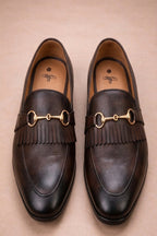 pair of brown horsebit loafers possibly made of leather or synthetic leather,featuring a gold-tone buckle detail and fringe