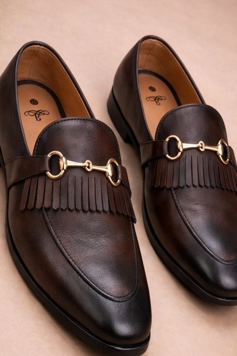 pair of brown horsebit loafers possibly made of leather or synthetic leather,featuring a gold-tone buckle detail and fringe