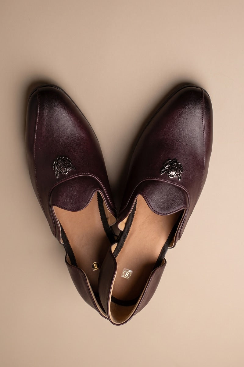 Brown glossy juttis for featuring a metallic crest embellishment