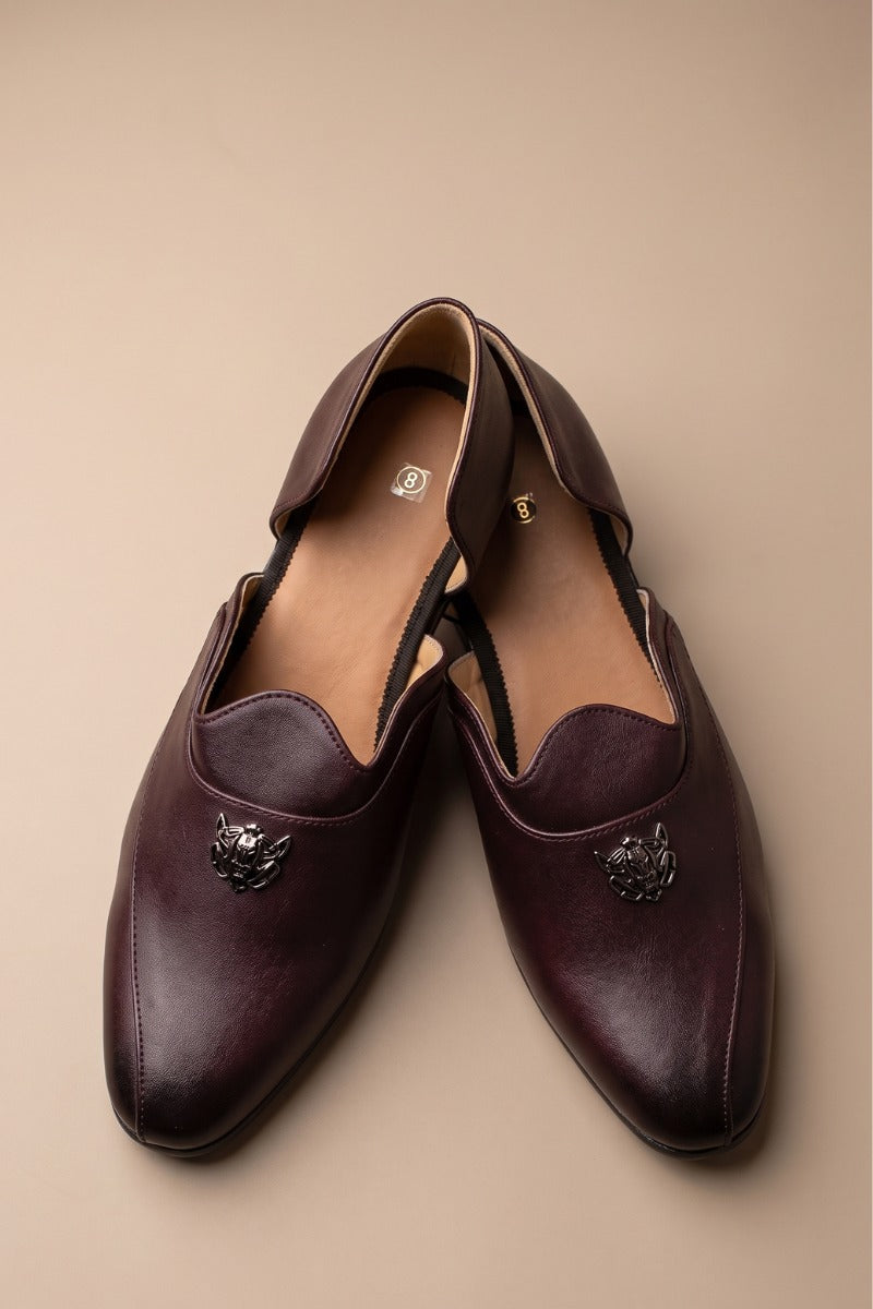 Brown glossy juttis for featuring a metallic crest embellishment