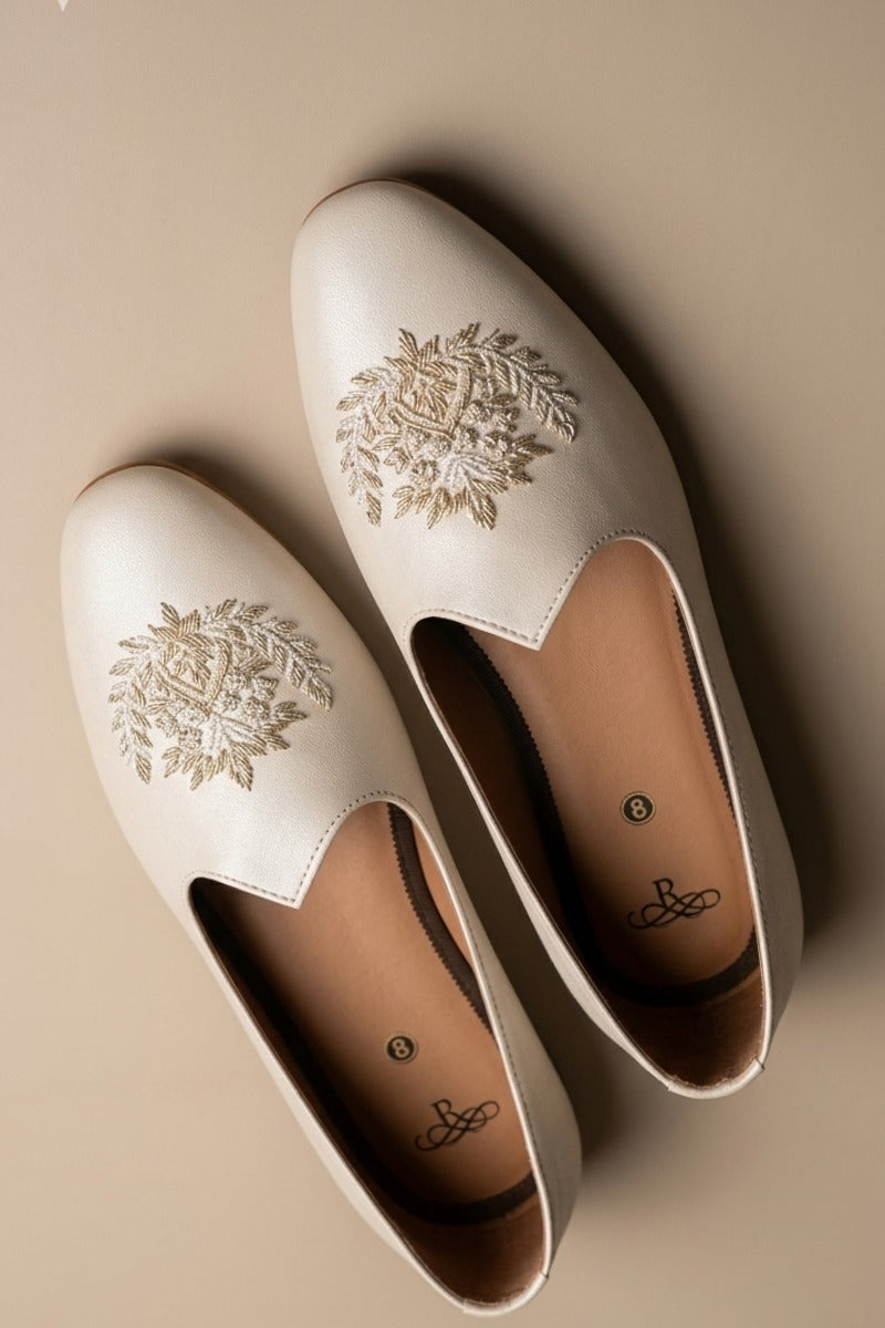 Cream colour juttis with intricate silver and crest -inspired embroidery