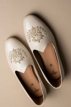 Cream colour juttis with intricate silver and crest -inspired embroidery