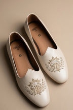 Cream colour juttis with intricate silver and crest -inspired embroidery